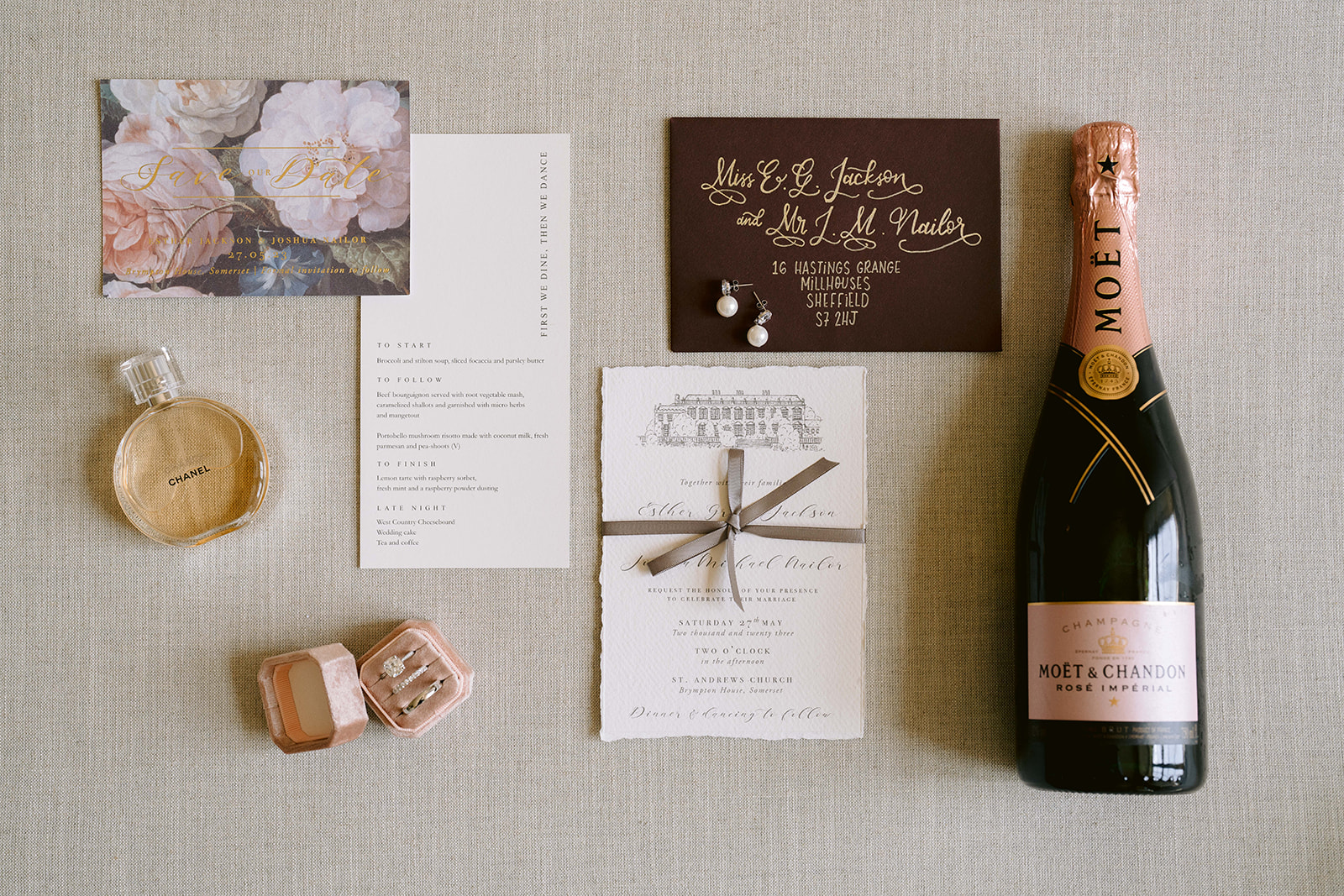 flat lay photo of brides details including rings champagne invites and perfume