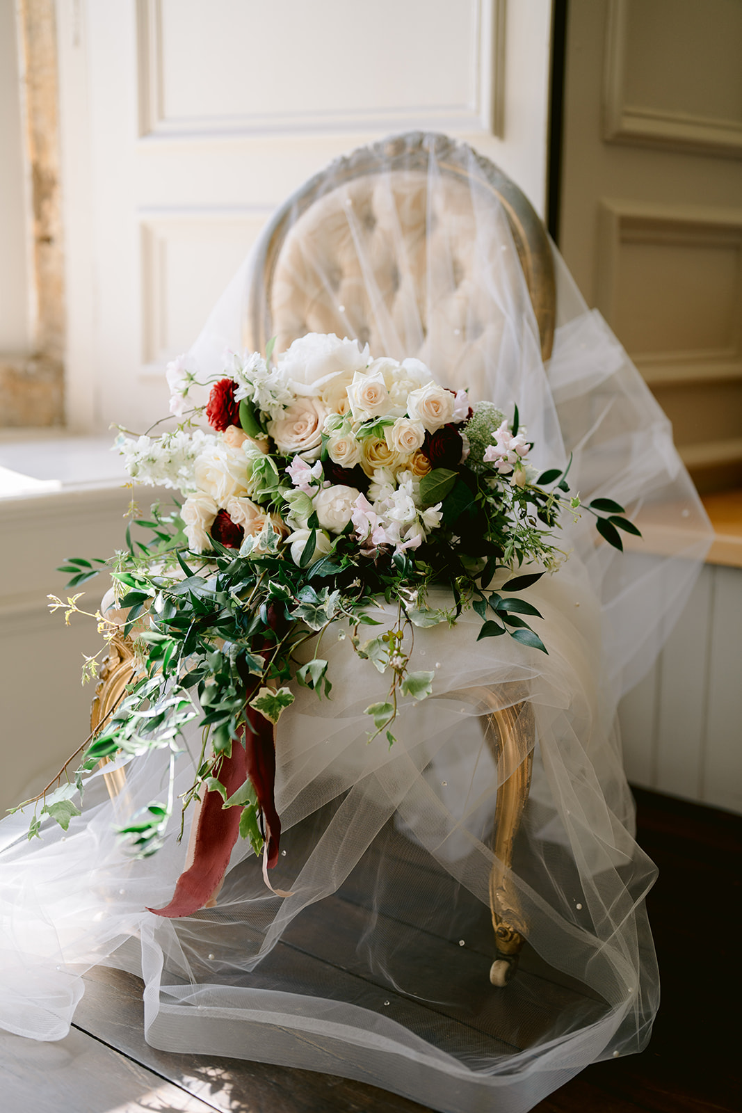 the wedding bouquet is on a vintage french chair and the wedding veil. The bouquet has roses camelia's and ivy ribbons