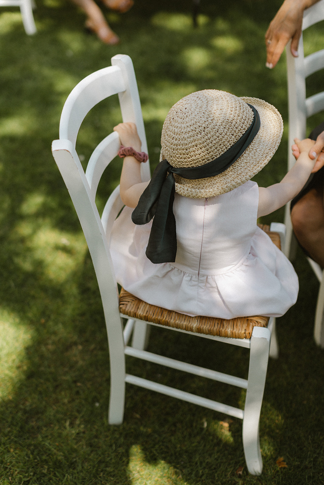 kleines Mädchen mit Hut und Band sitzt auf einem Stuhl