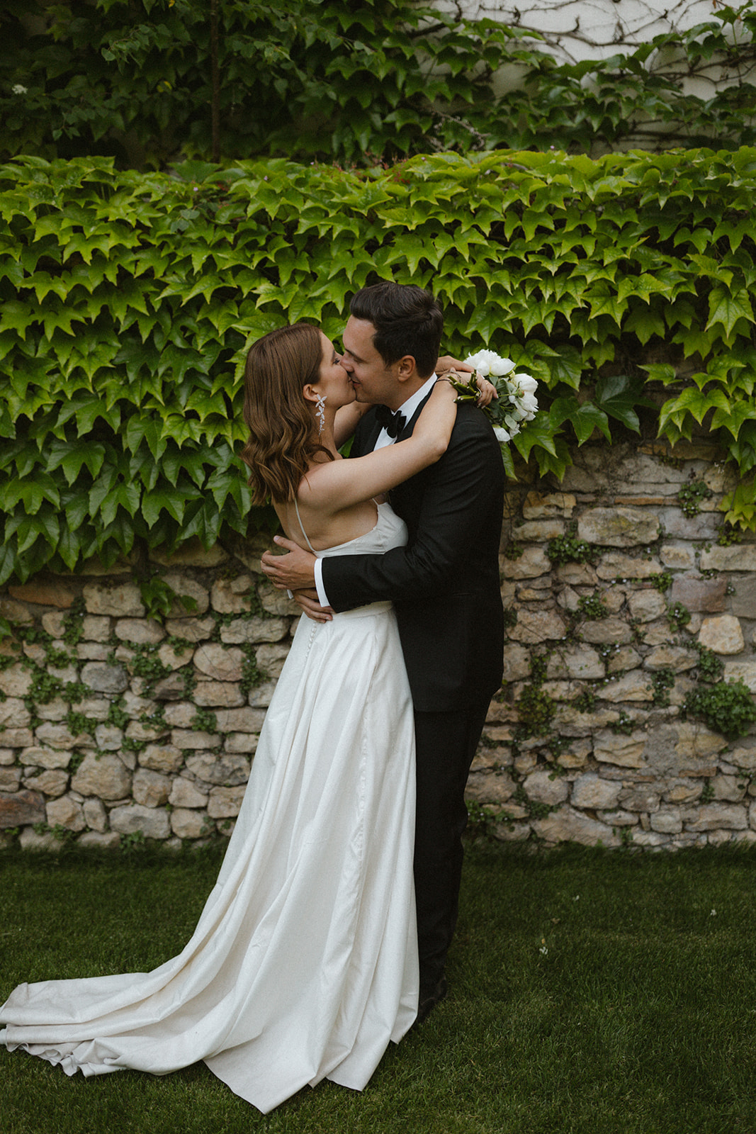 elegantes Brautpaar küsst sich vor Efeu im Garten von Weingut Boudier Koeller