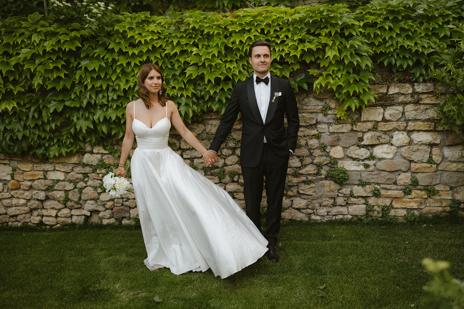 elegantes Brautpaar hält sich an den Händen vor Efeu im Garten von Weingut Boudier Koeller