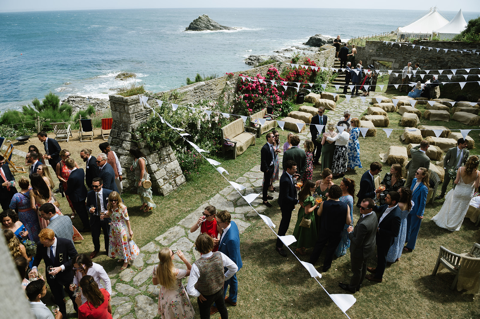 Wedding guests mingling in the garden at Porth-en-Alls with the blue sea and sky in the background