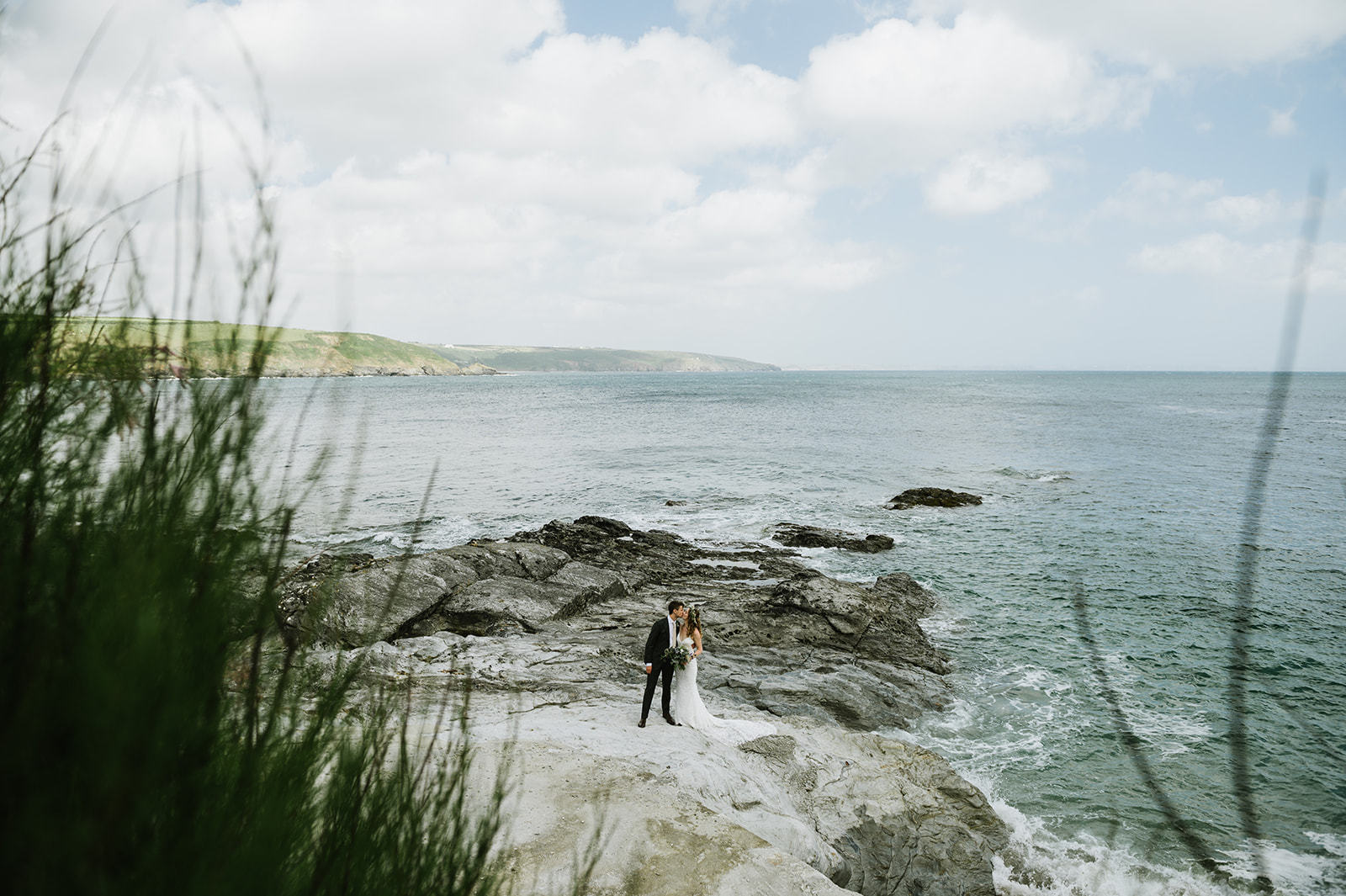 the bride and groom on the beach in Cornwall with the turquoise sea and blue sky behind them