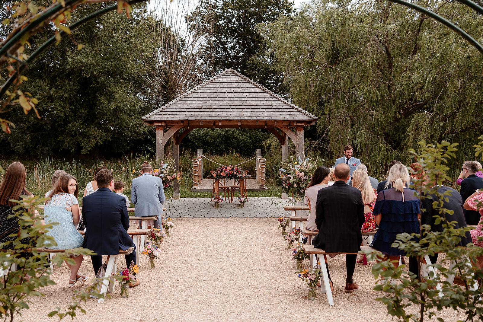 All the guests seated by the outdoor wedding pergola at a summer wedding at Silchester Farm