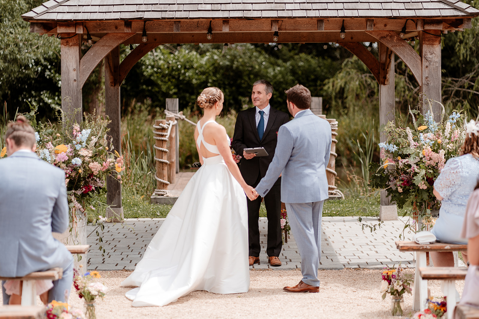 Bride and groom hold hands in front of their officiant at a summer wedding at Silchester Farm