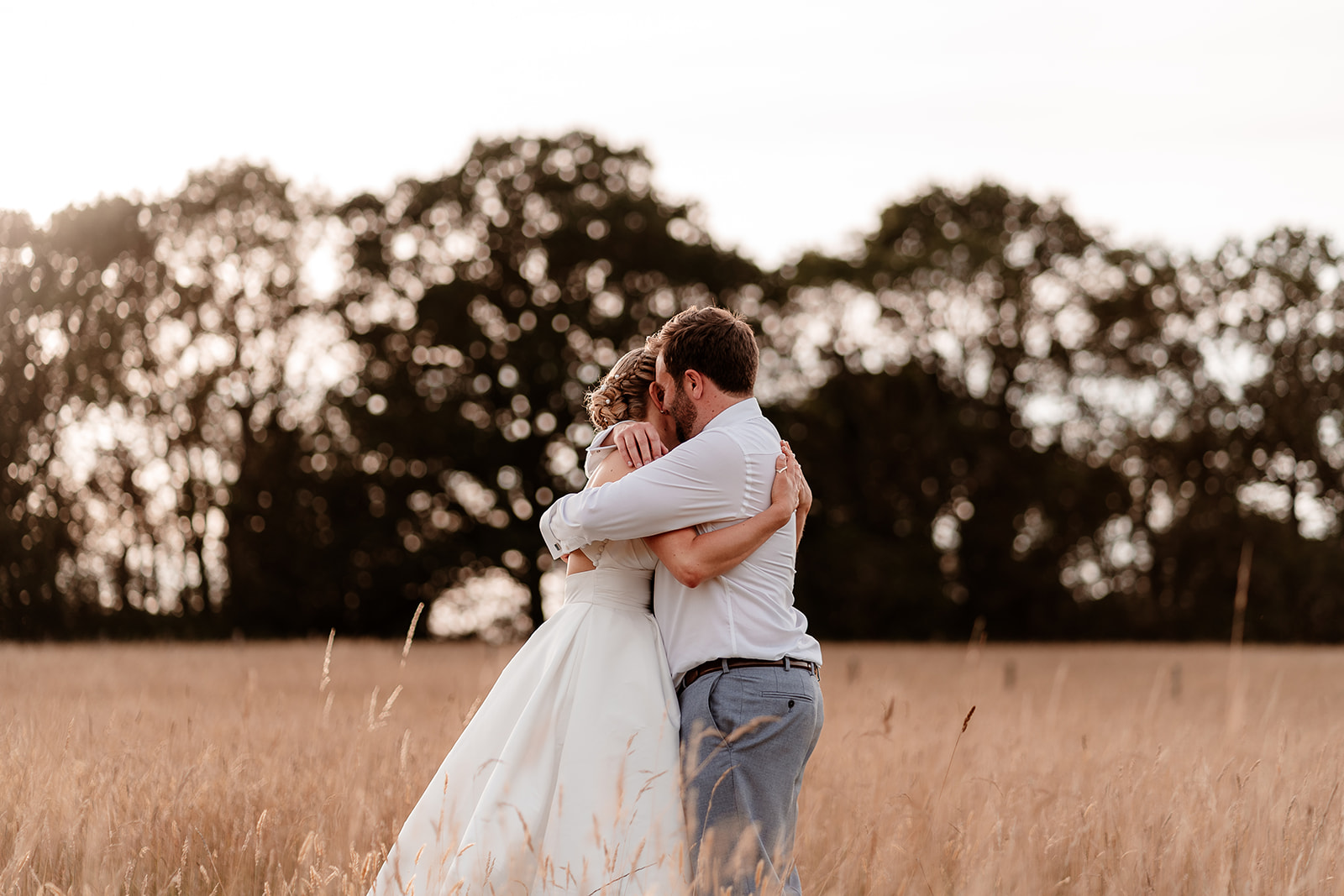 Bride and groom hug together in the golden field at sunset at a summer wedding at Silchester Farm