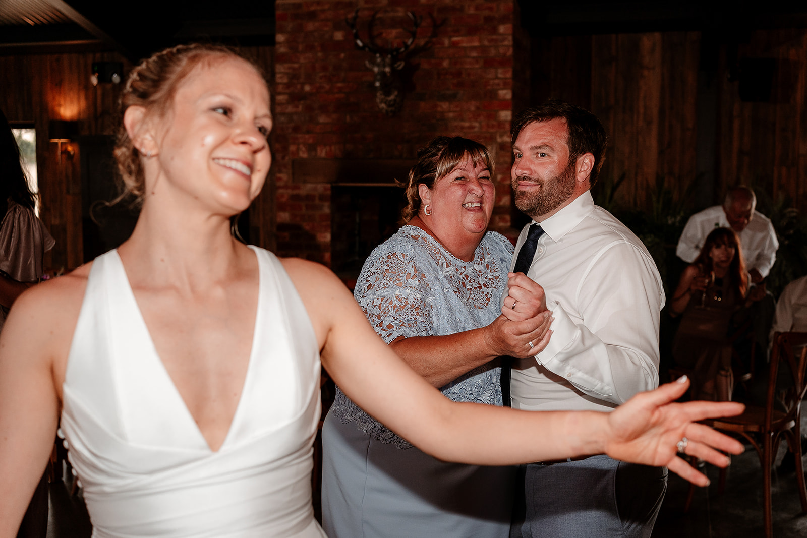 Bride smiles while her husband dances with his mum in the background at a summer wedding at Silchester Farm