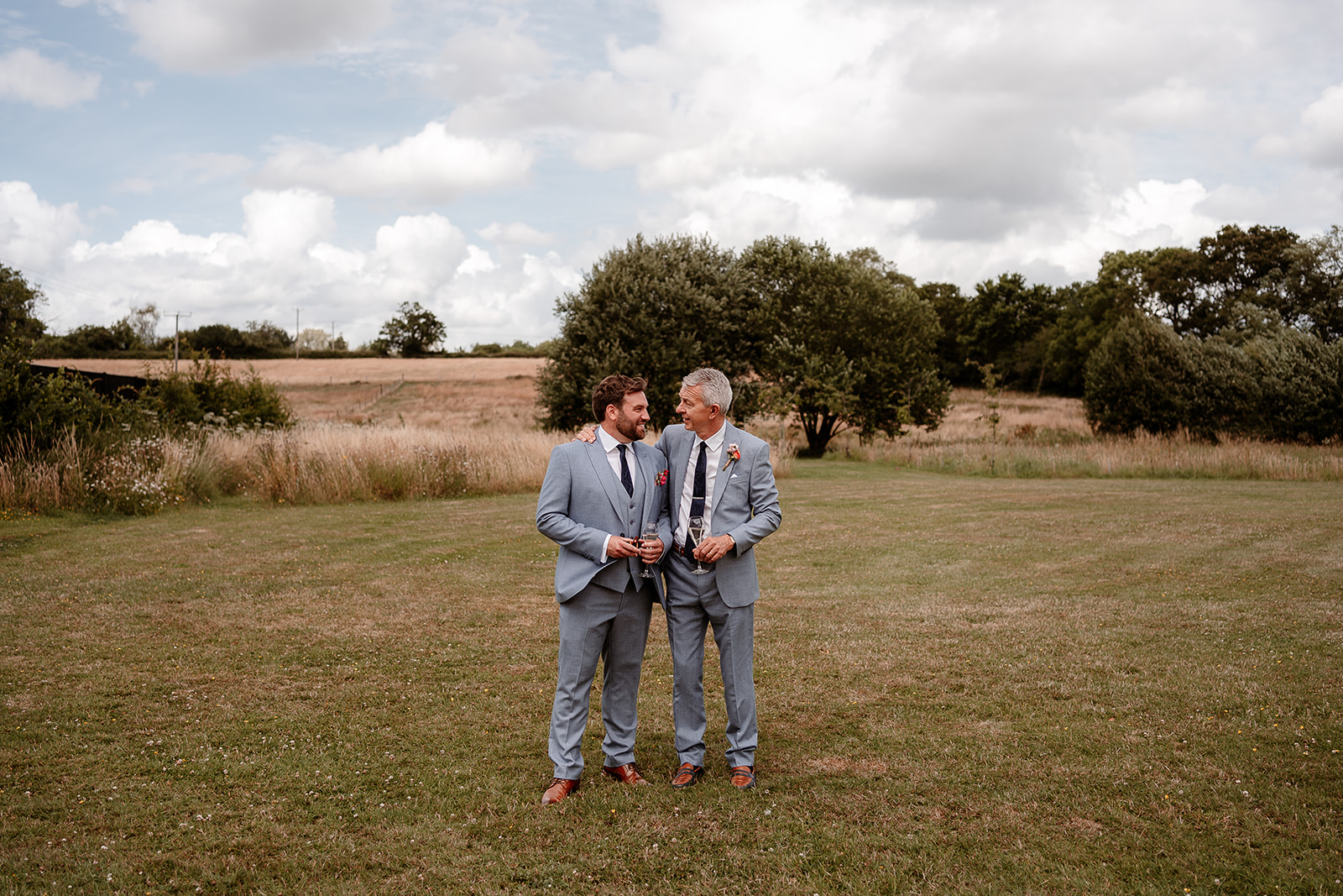 Groom and father of the bride share a hug in the gardens of Silchester Farm in the summer sunshine