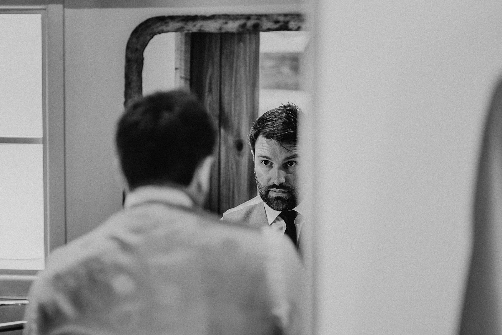 Groom does his tie in the mirror at a summer wedding at Silchester Farm