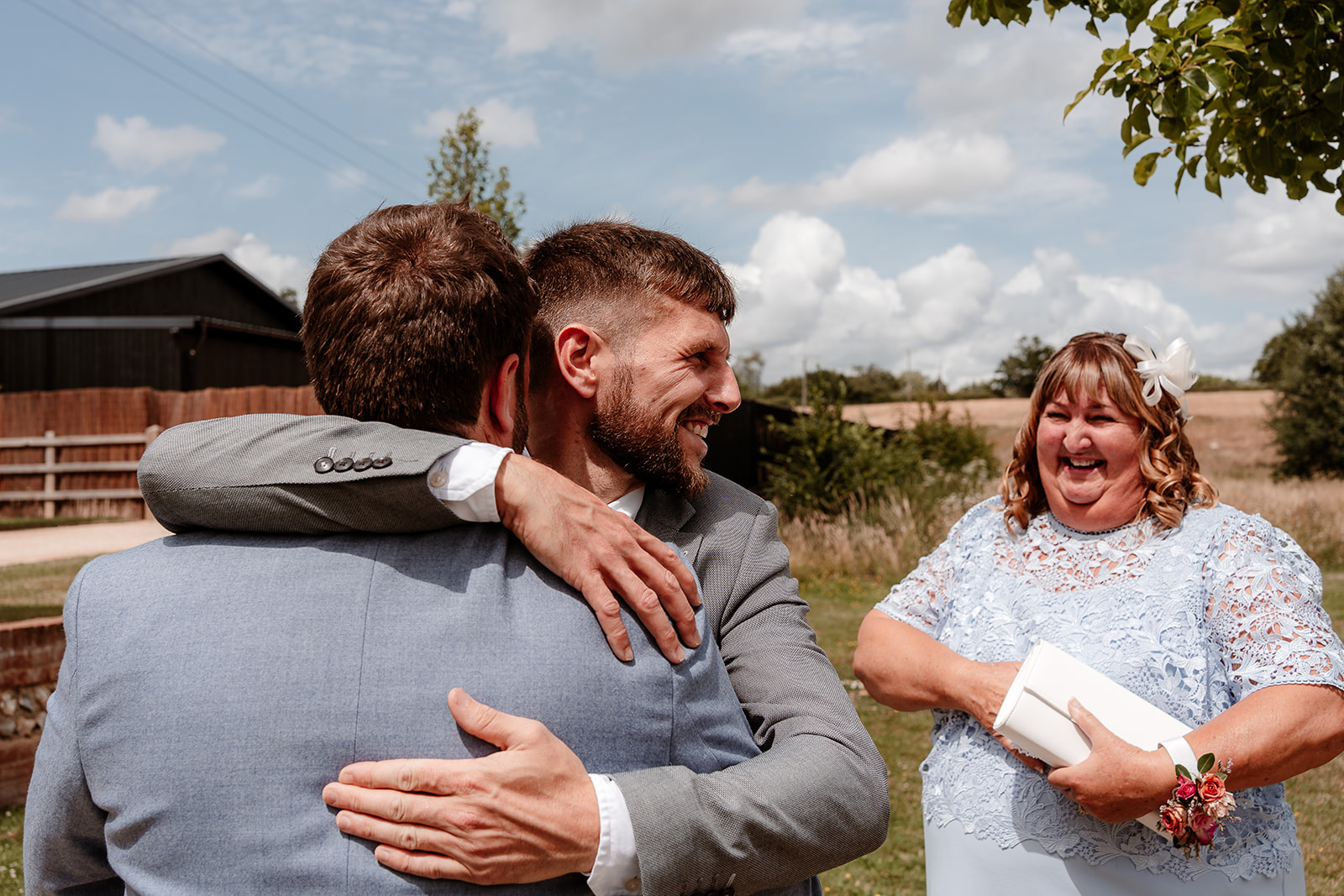 Groom is hugged by his brother as their mum smiles in the background at a summer wedding at Silchester Farm