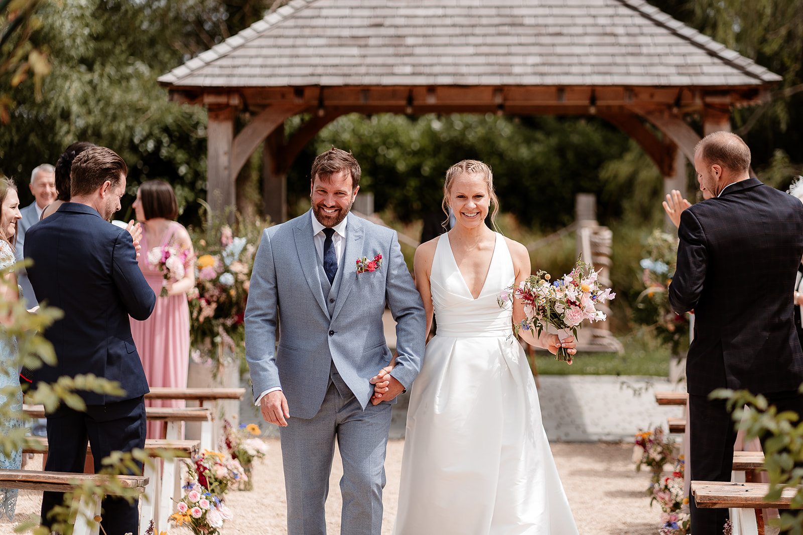 Joyful bride and groom walk out of their ceremony together at a summer wedding at Silchester Farm