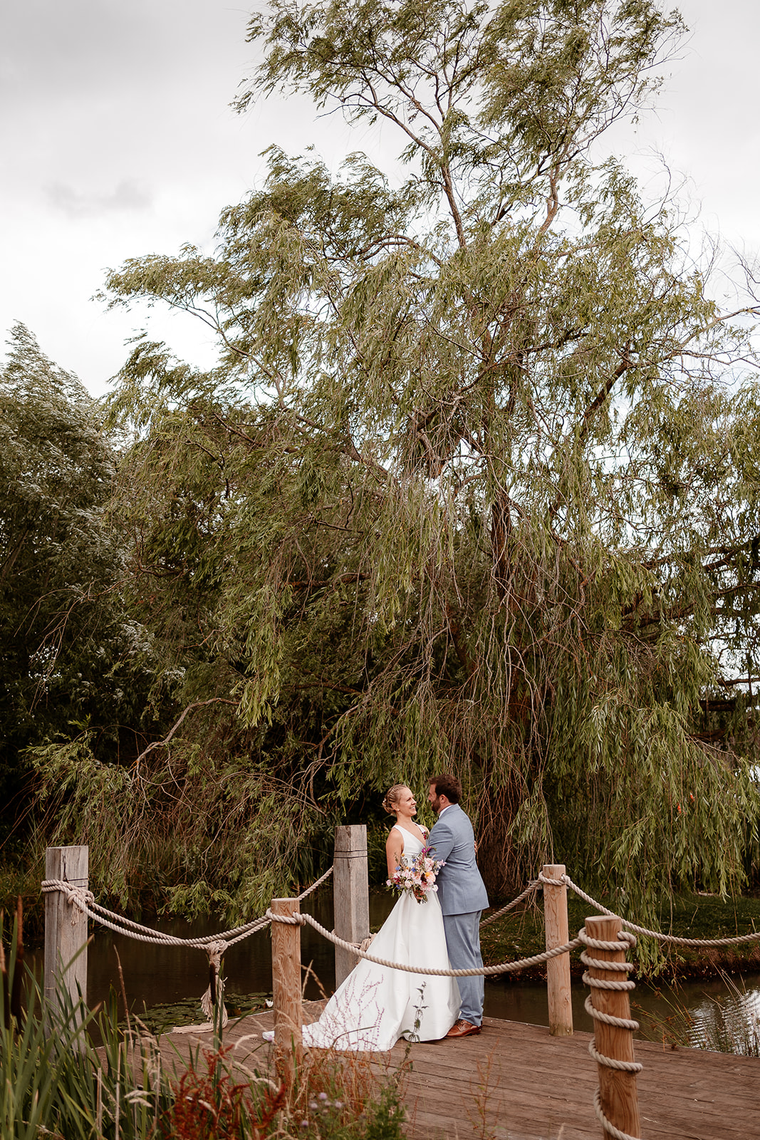 Portrait photo of the bride and groom cuddling by the willow tree at a summer wedding at Silchester Farm