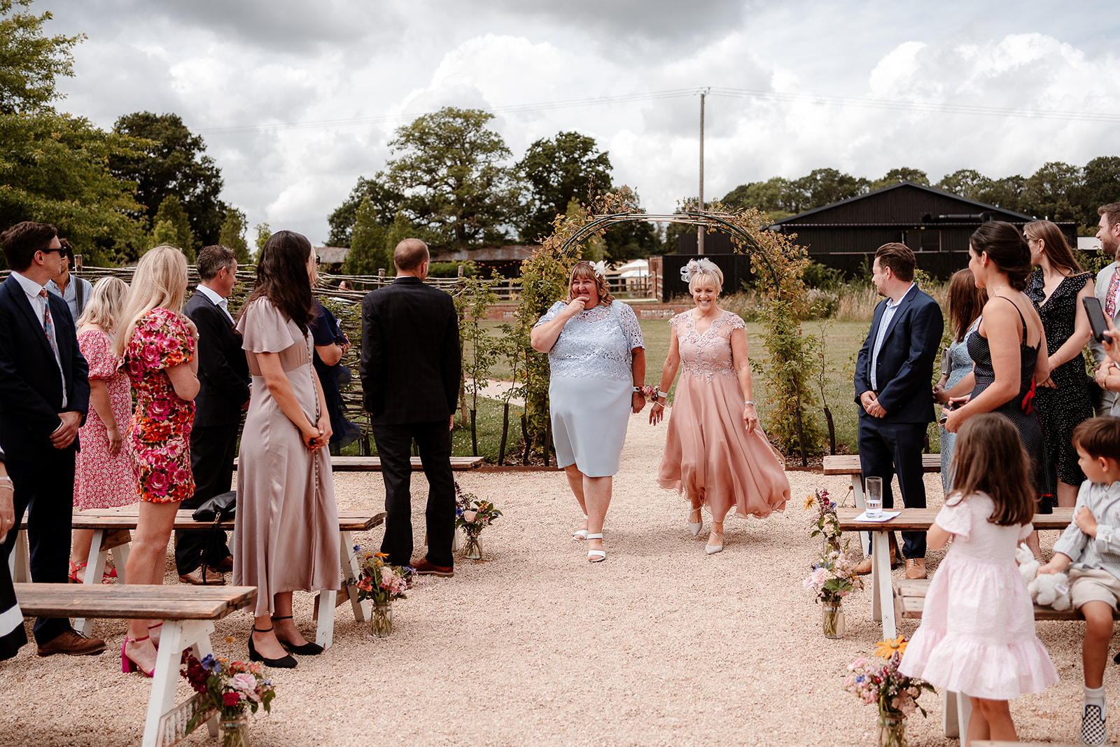 The mothers of the bride and groom walk down the aisle together at a summer wedding at Silchester Farm