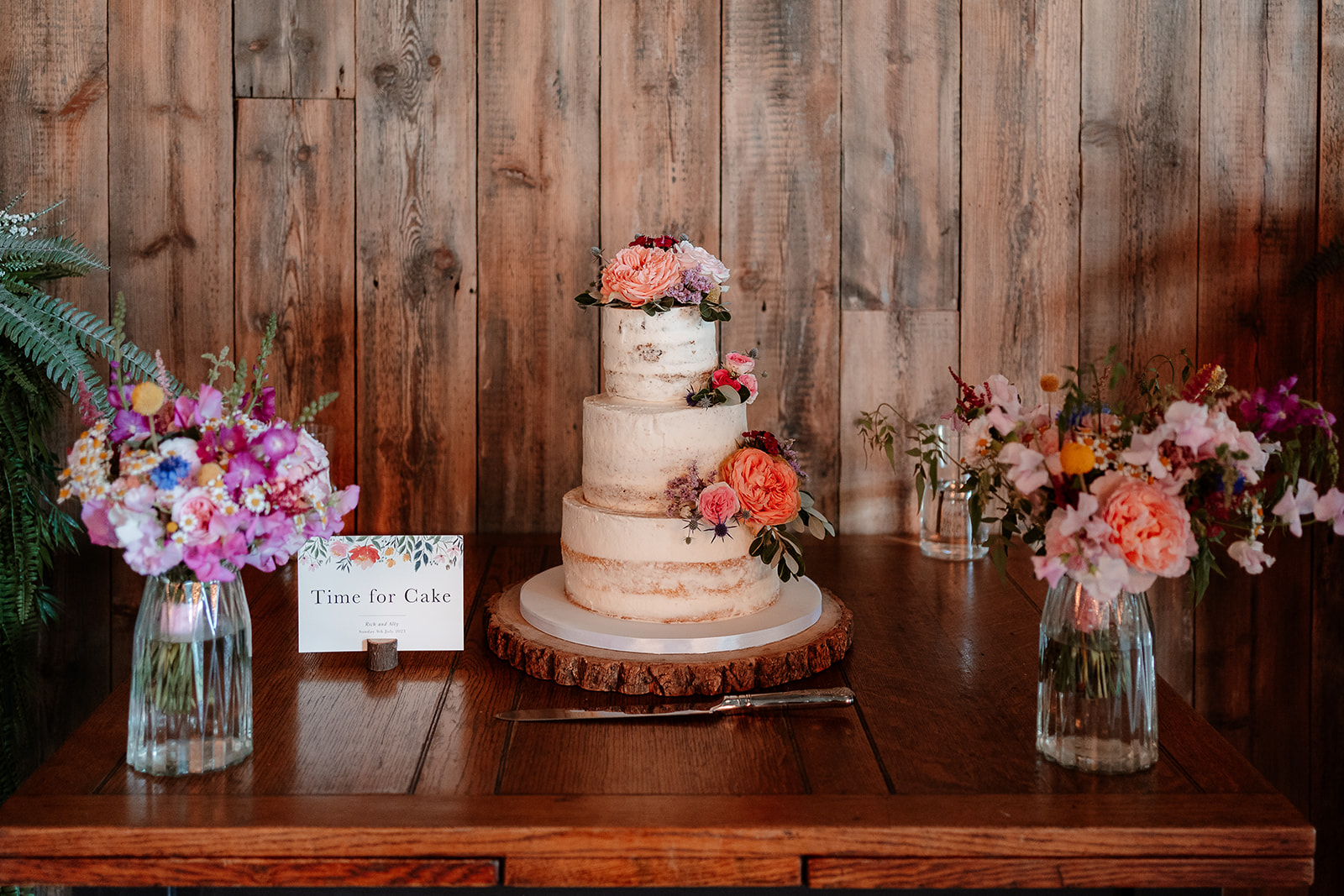 Wedding cake surrounded by brightly coloured flowers at a summer wedding at Silchester Farm