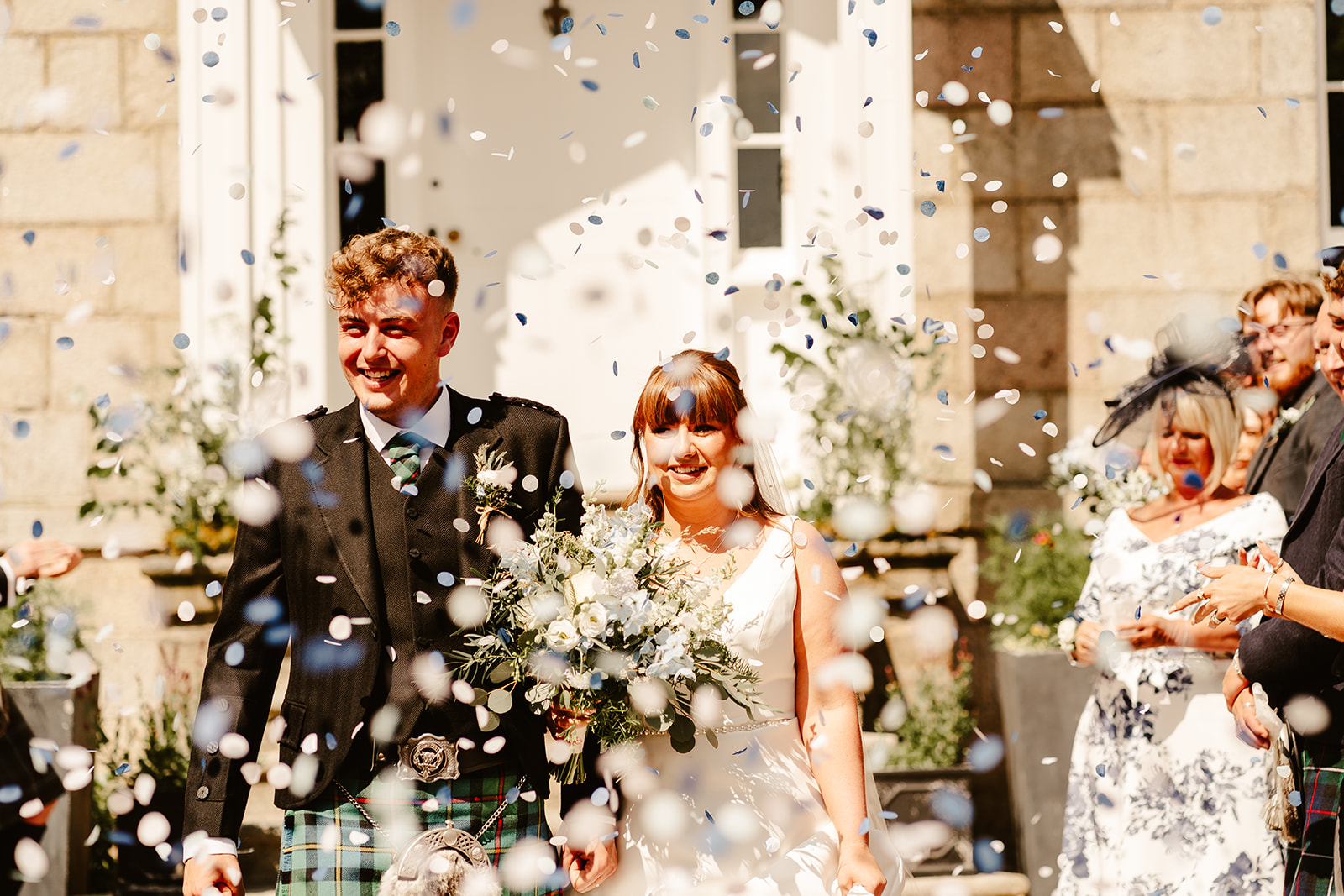 Couple laughing as guests shower them with confetti outside of Elrick House Wedding Venue
