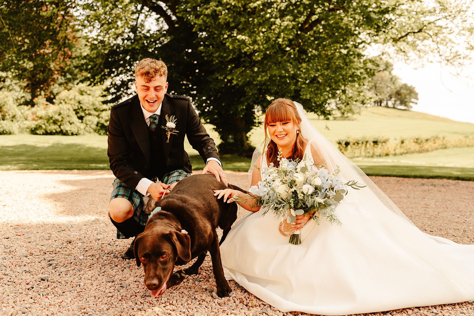 Couple crouching down with their dog, laughing outside of Elrick House Wedding Venue