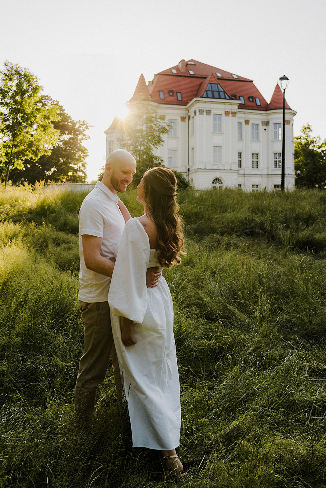 Para narzeczonych przytula się podczas sesji zdjęciowej w promieniach zachodzącego słońca. W tle Zamek w Leśnicy.
