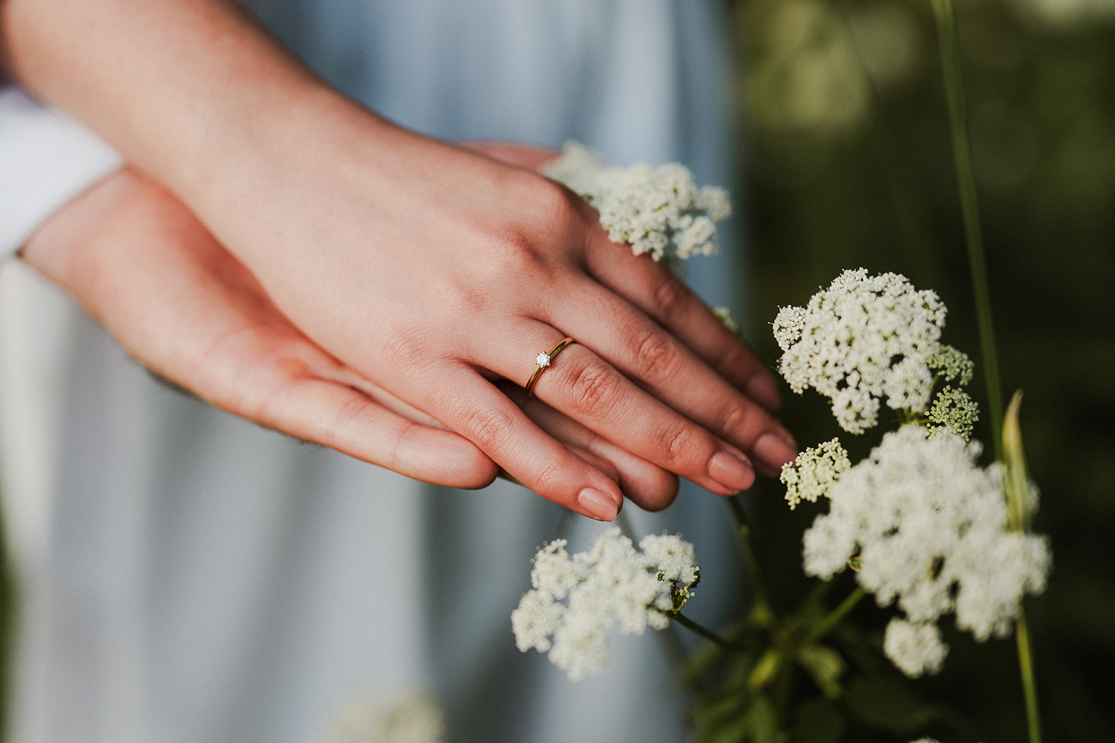 Zbliżenie na dłonie narzeczonych pośród kwiatów. Na palcu widoczny jest pierścionek zaręczynowy
