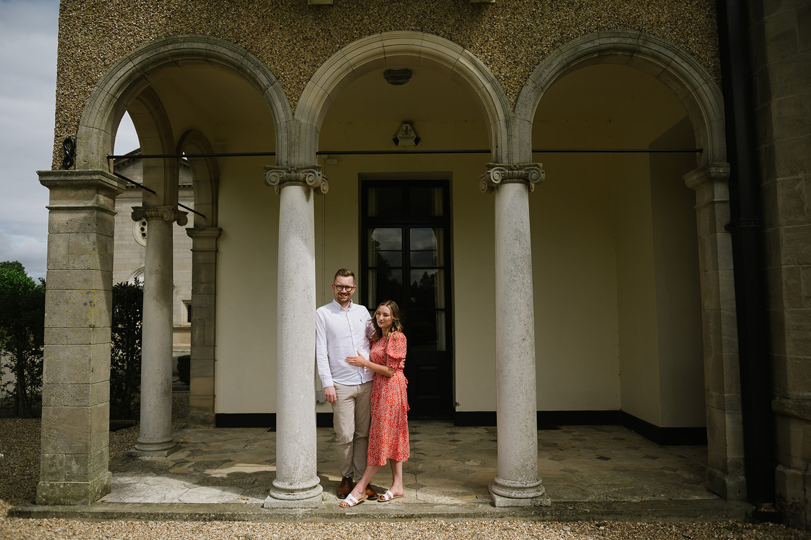 A couple pose under the arches at Bourton Hall for their engagement photos