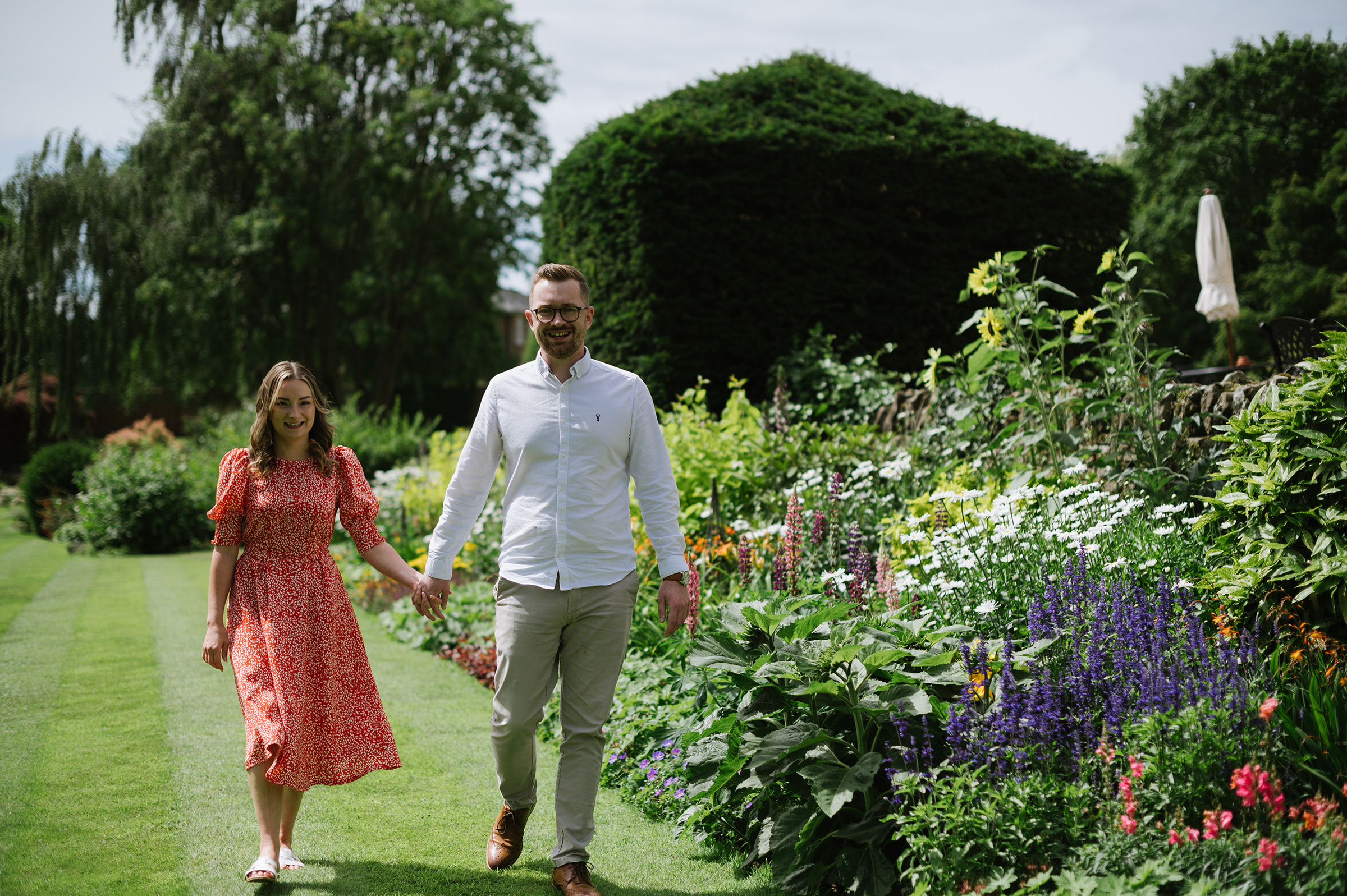 couple walk hand in hand through the flowers at Bourton Hall