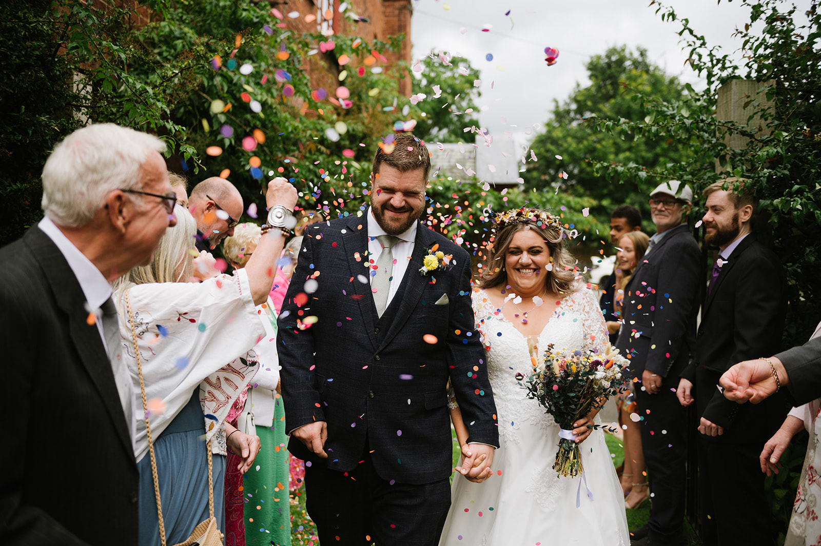 The bride and groom walking through a flurry of colourful confetti in the garden at Hundred House Hotel