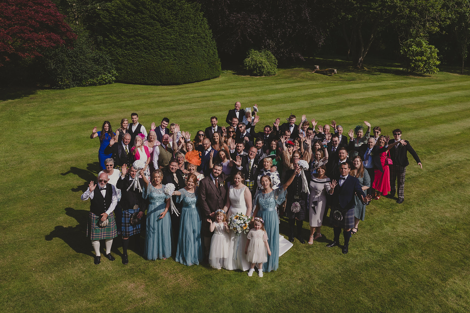An aerial group photos of the wedding guests standing together on the grounds of Elsick House waving to the camera.