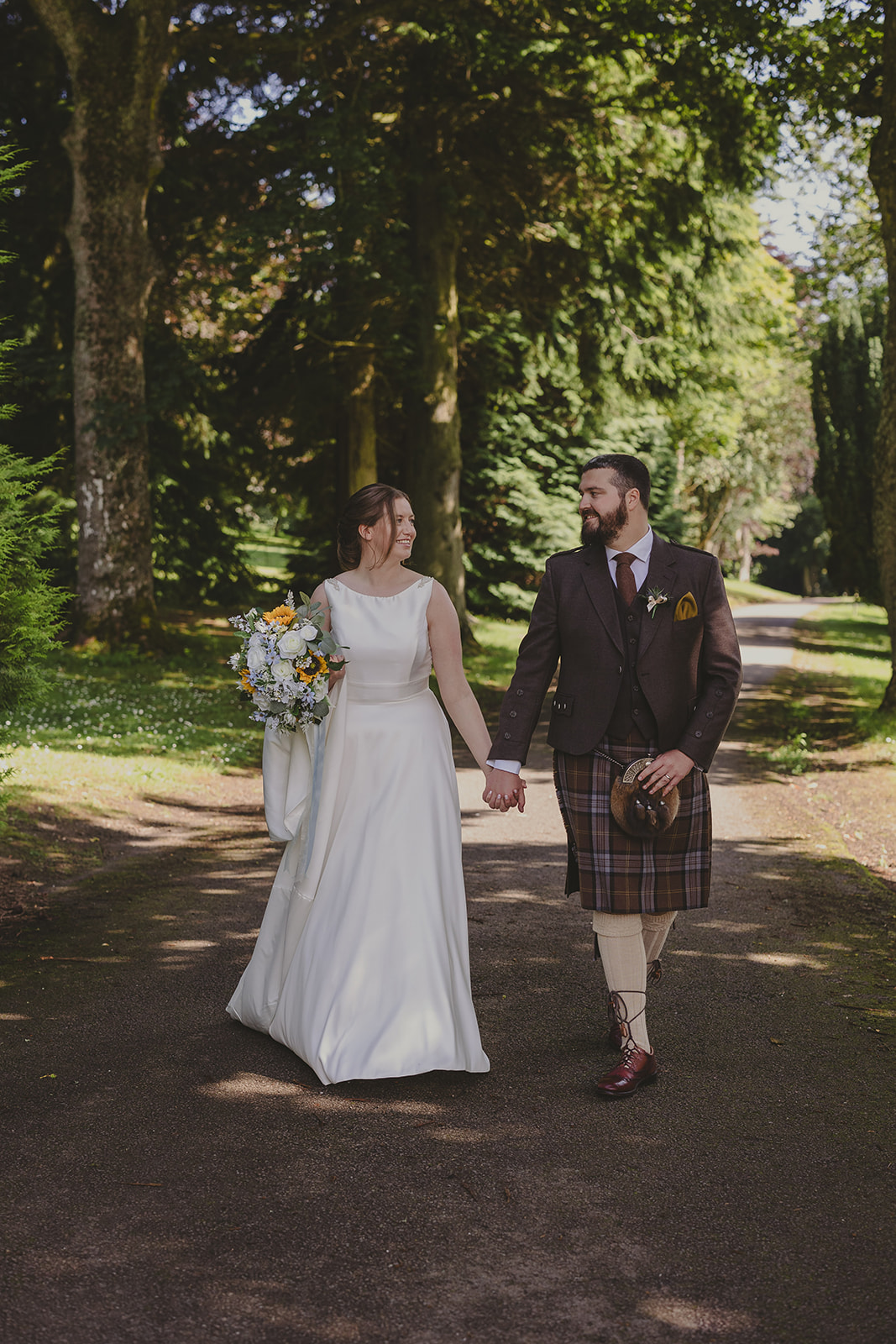 A bride and groom walking hand in hand around the grounds of Elsick House on their wedding day in Scotland.