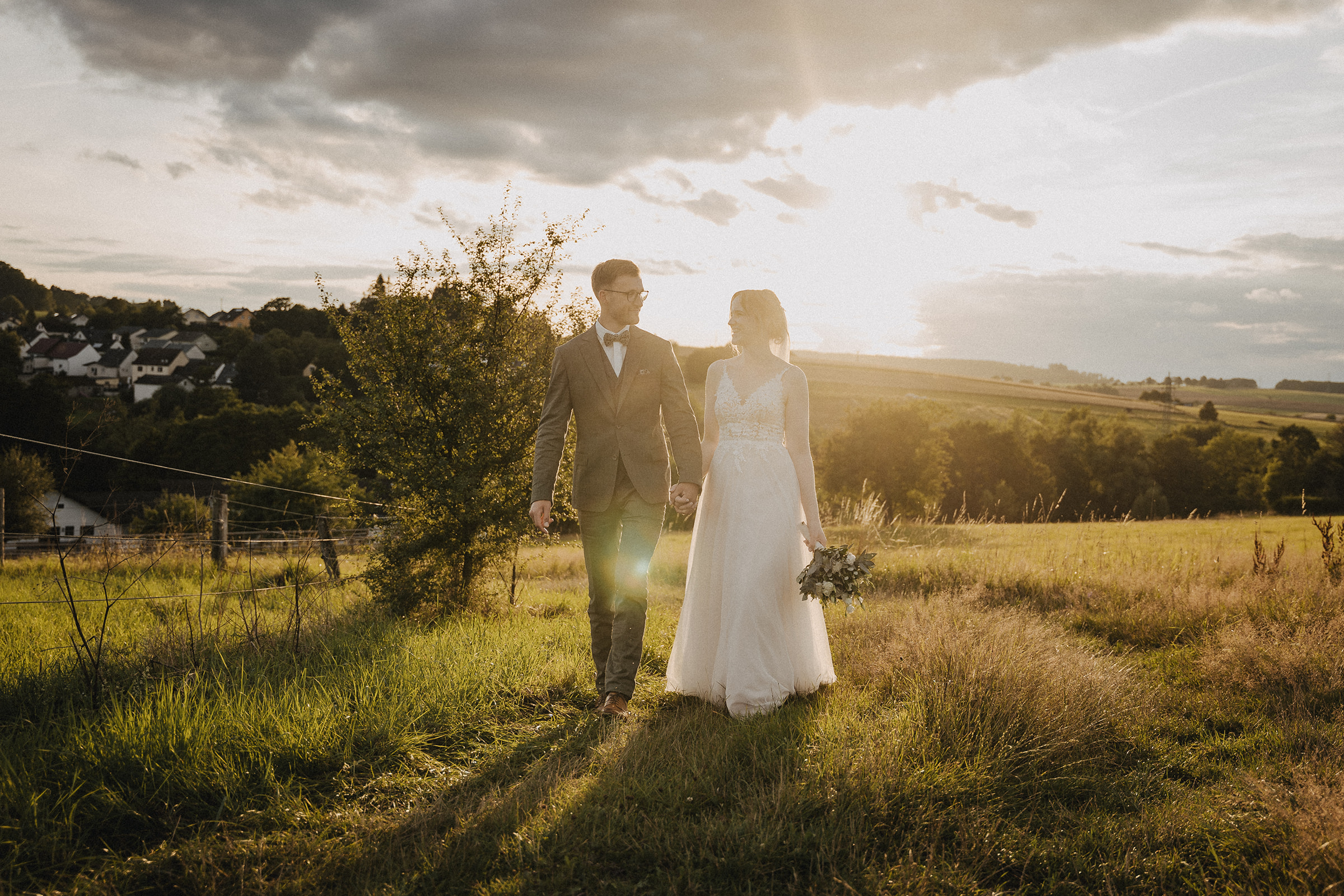 Ein Brautpaar in der Abendsonne geht Hand in Hand über eine Wiese oberhalb der Krambergsmühle