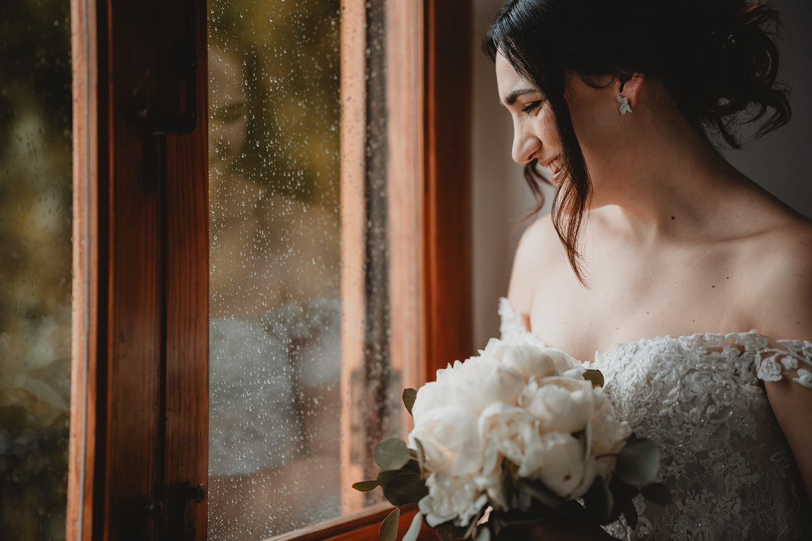 Sposa che guarda la pioggia dalla finestra durante il giorno de suo matrimonio