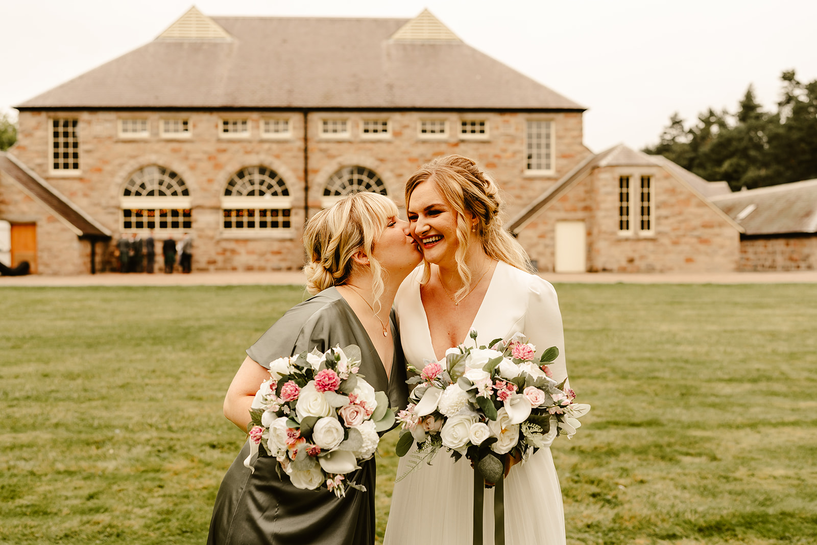 Bride standing with her bridesmaid who is wearing a sage green dress