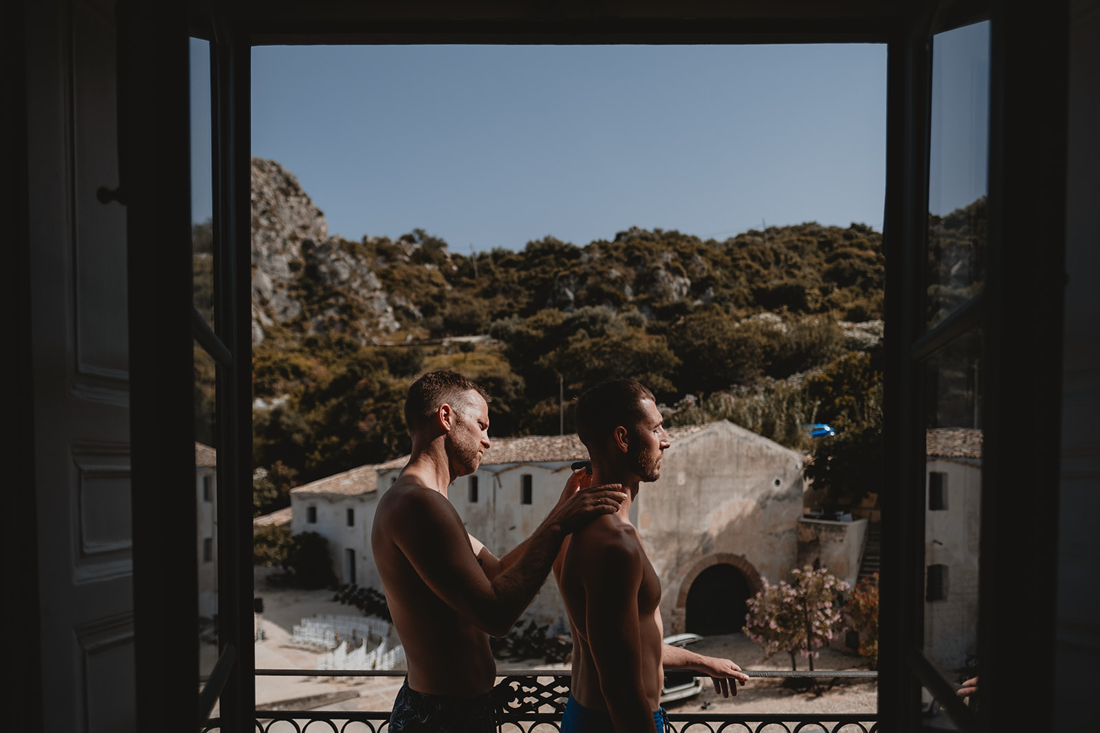 Couple of boys getting ready in front of the window of a room in the Tonnara di Scopello