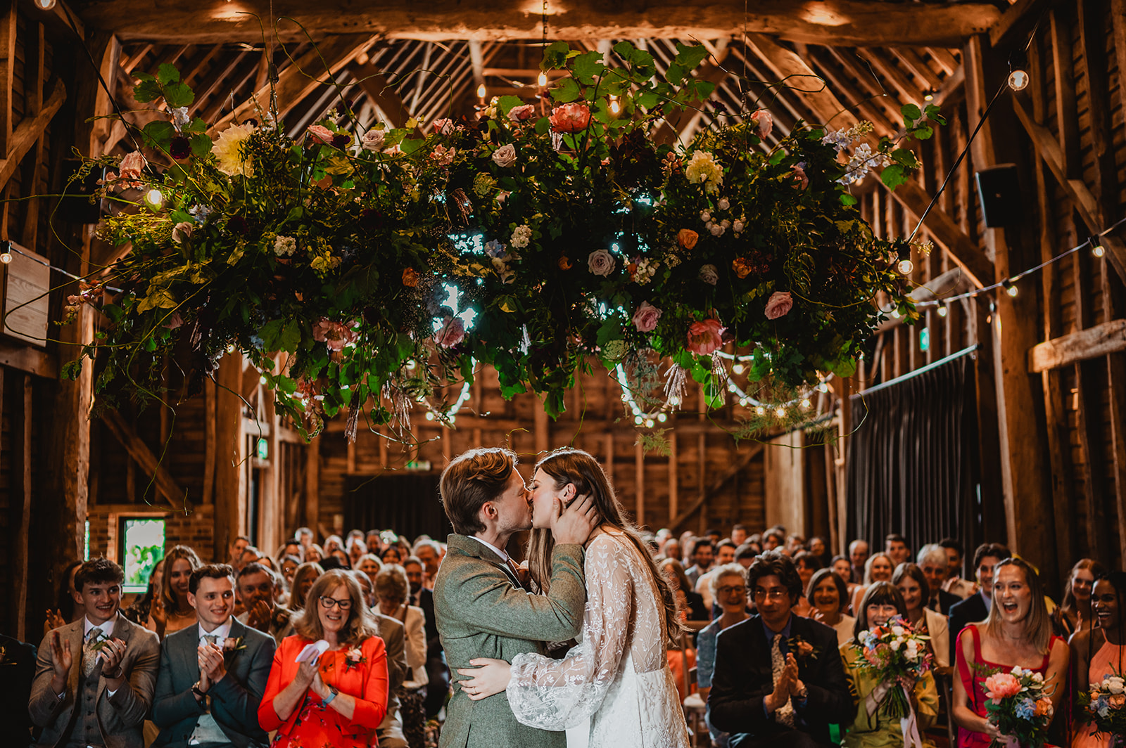 A bride and groom share a first kiss under some flowers at Barns at Redcoats