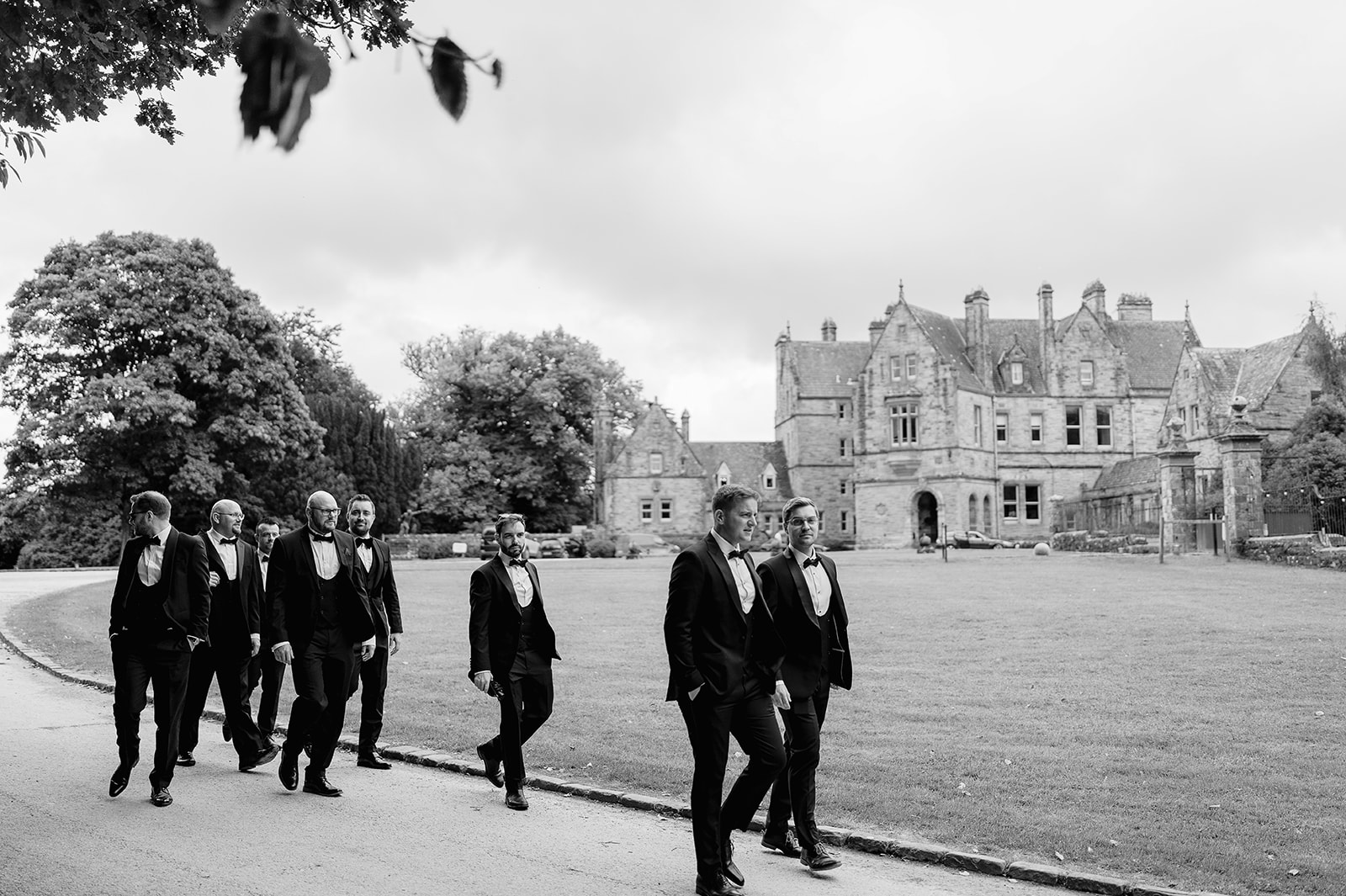 black and white photo of groomsmen walking with castle leslie in the background