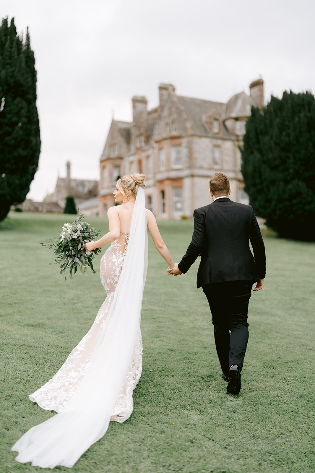 bride and groom walking to castle leslie with veil behind 