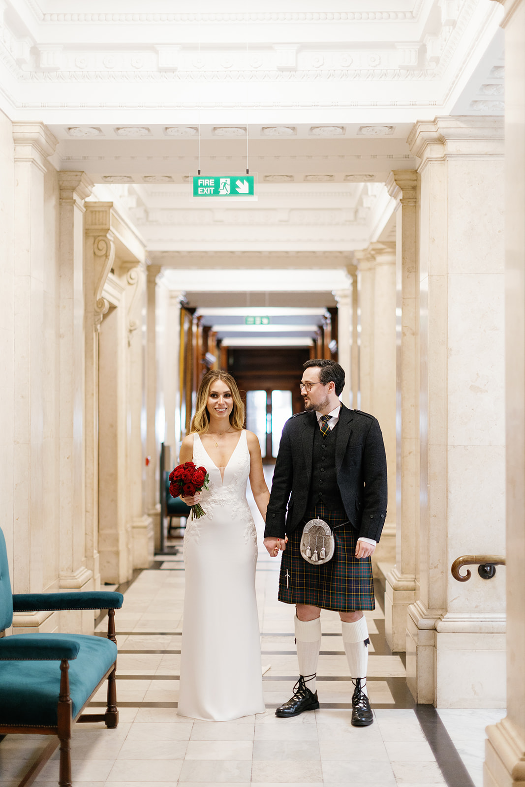 long shot of bride and groom hold hands in the hallway