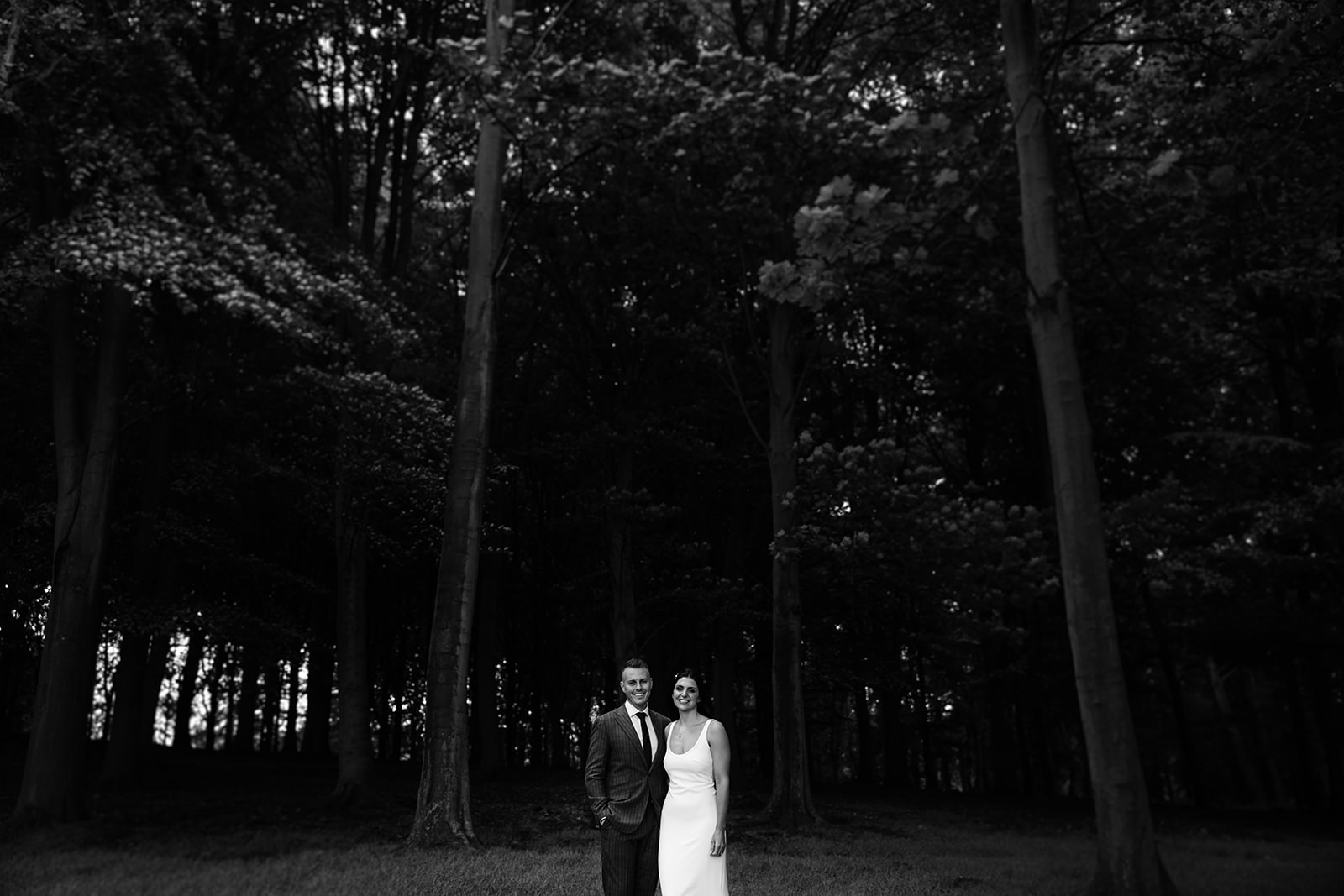 a black and white photo of the bride and groom stood in the woods near to The Hovels Wedding Venue