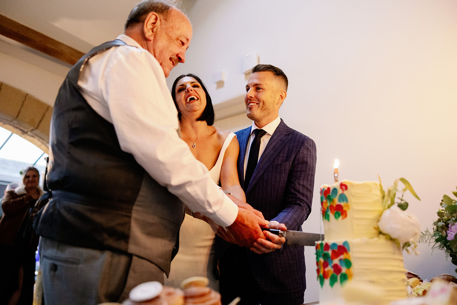 bride, groom and grandad cutting their shared wedding and birthday cake