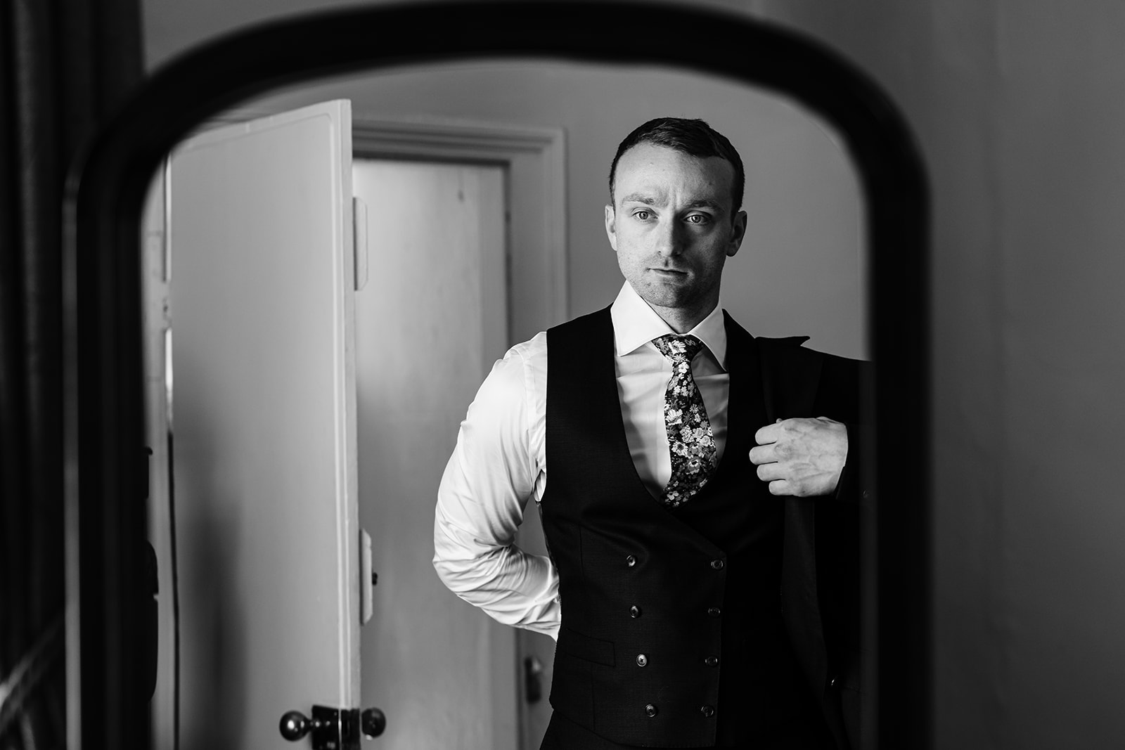 Groom putting on his suit jacket in a mirror 