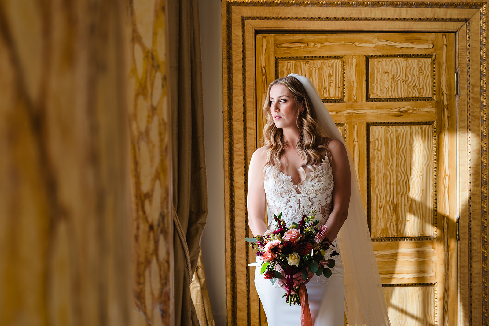 Brid e with her bright wedding bouquet looking out the window at Gosfield hall