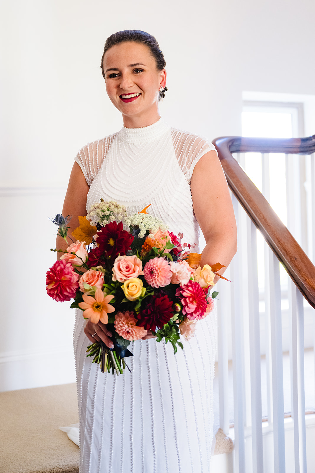 Bride standing on the staircase at home with her bright wedding bouquet