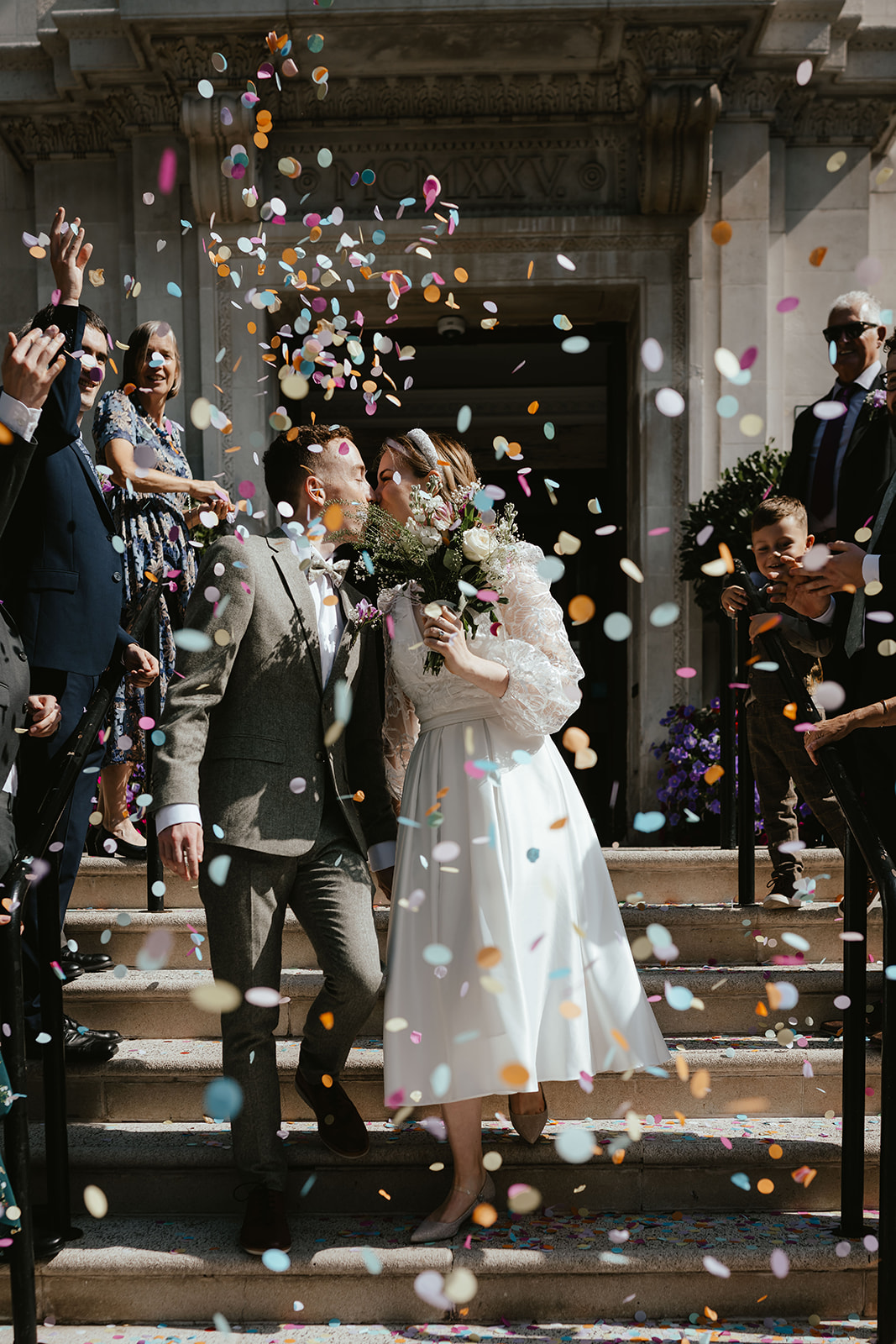 Portrait of Alex and Christina welcomed with confetti toss  while kissing at Islington Town Hall
