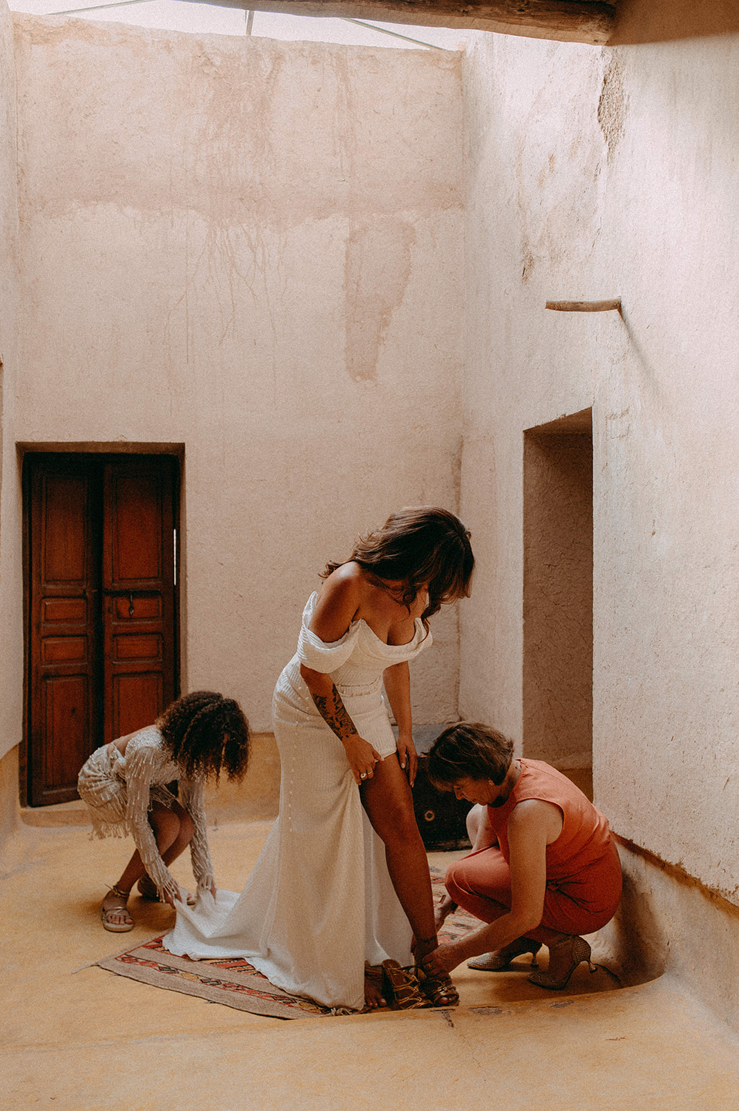 Une mariée dans sa robe Rime Arodaky pendant son habillage, entourée de sa mère et sa fille