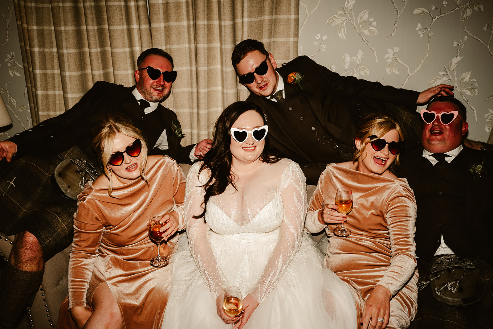 bridal party sit on sofa wearing heart-shaped sunglasses