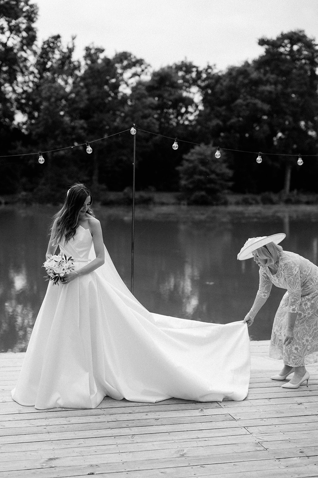 brides mum adjusting brides wedding dress in front of lake backdrop at barns and yard