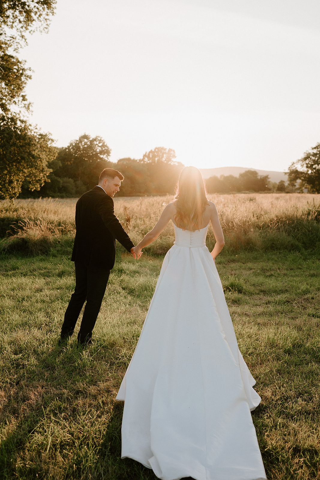 groom and bride walking into field with malvern hills at sunset at barns and yard 