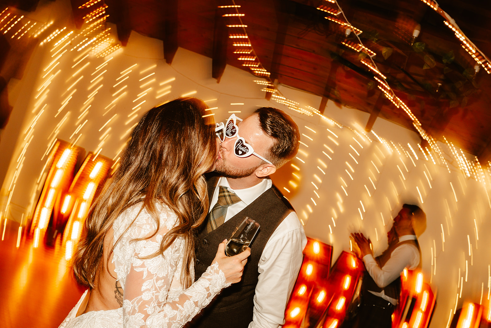 bride and groom kiss on dancefloor with fairy lights behind them