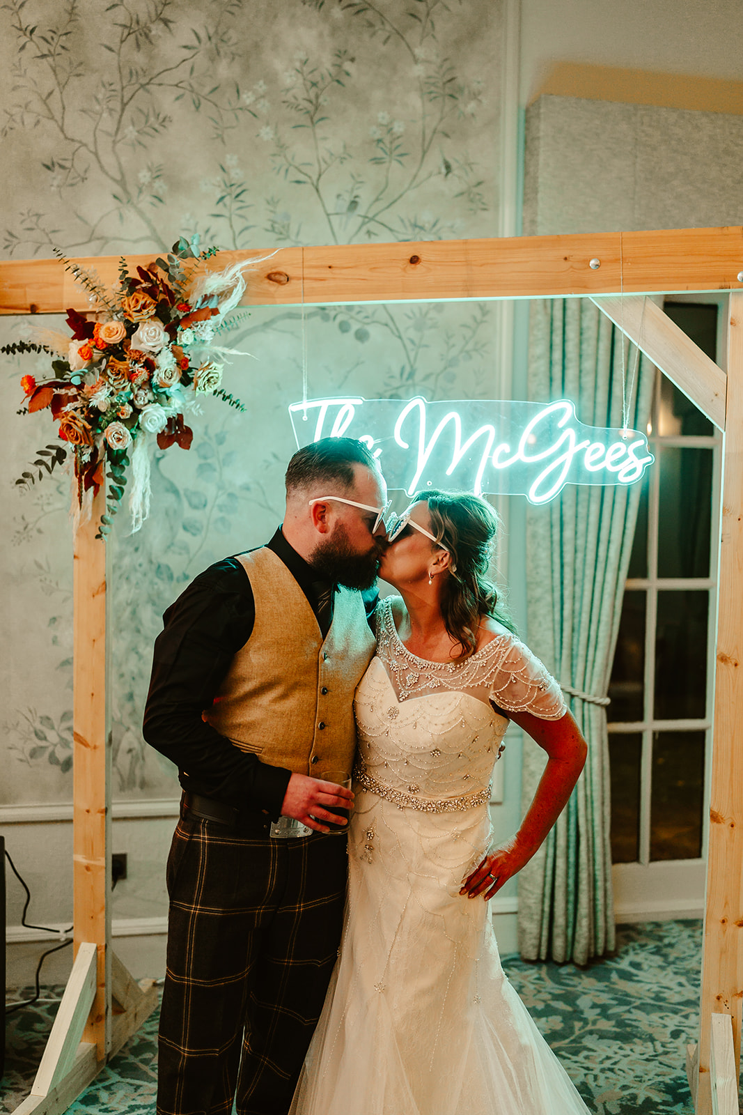 bride and groom kiss wearing sunglasses with a bespoke neon sign behind them