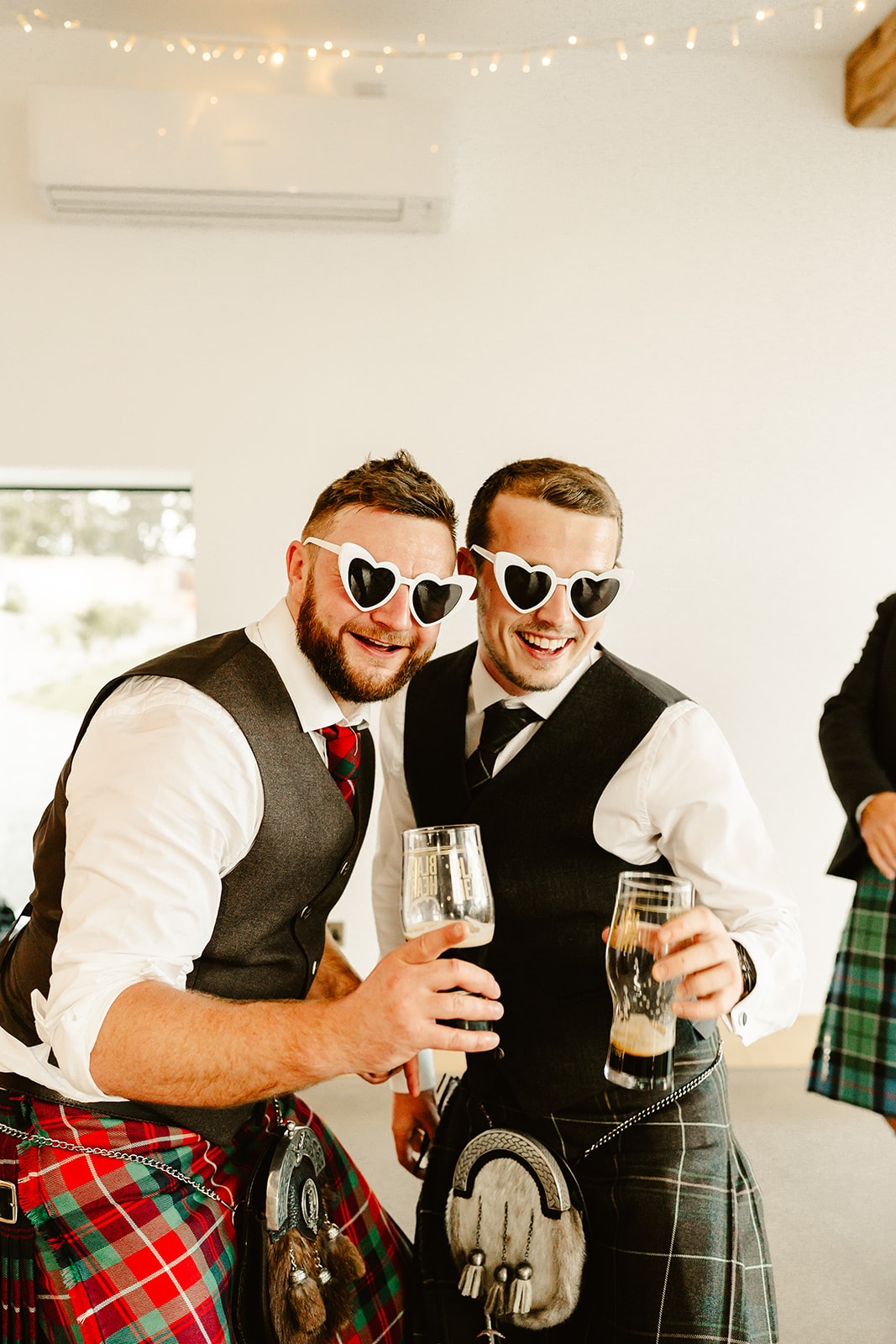 two men pose together on dancefloor as the hold drinks and wear heart shaped sunglasses at Schivas Steading wedding