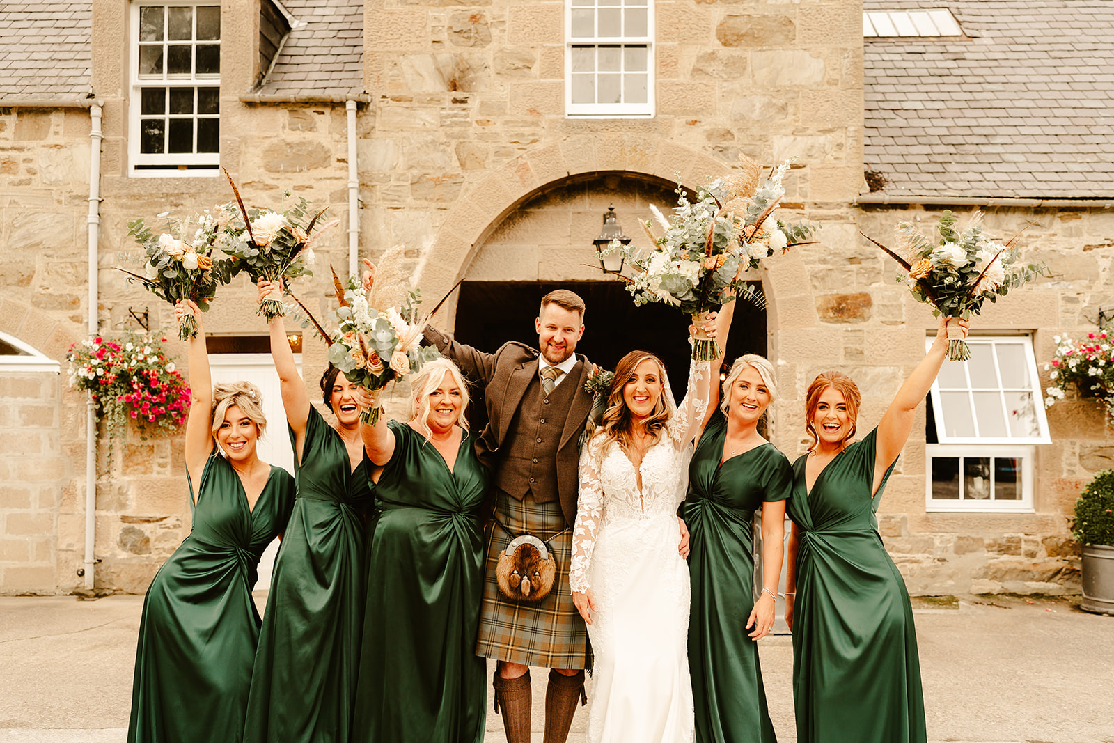 bridal party pose with hands in air in front of Aswanley wedding venue