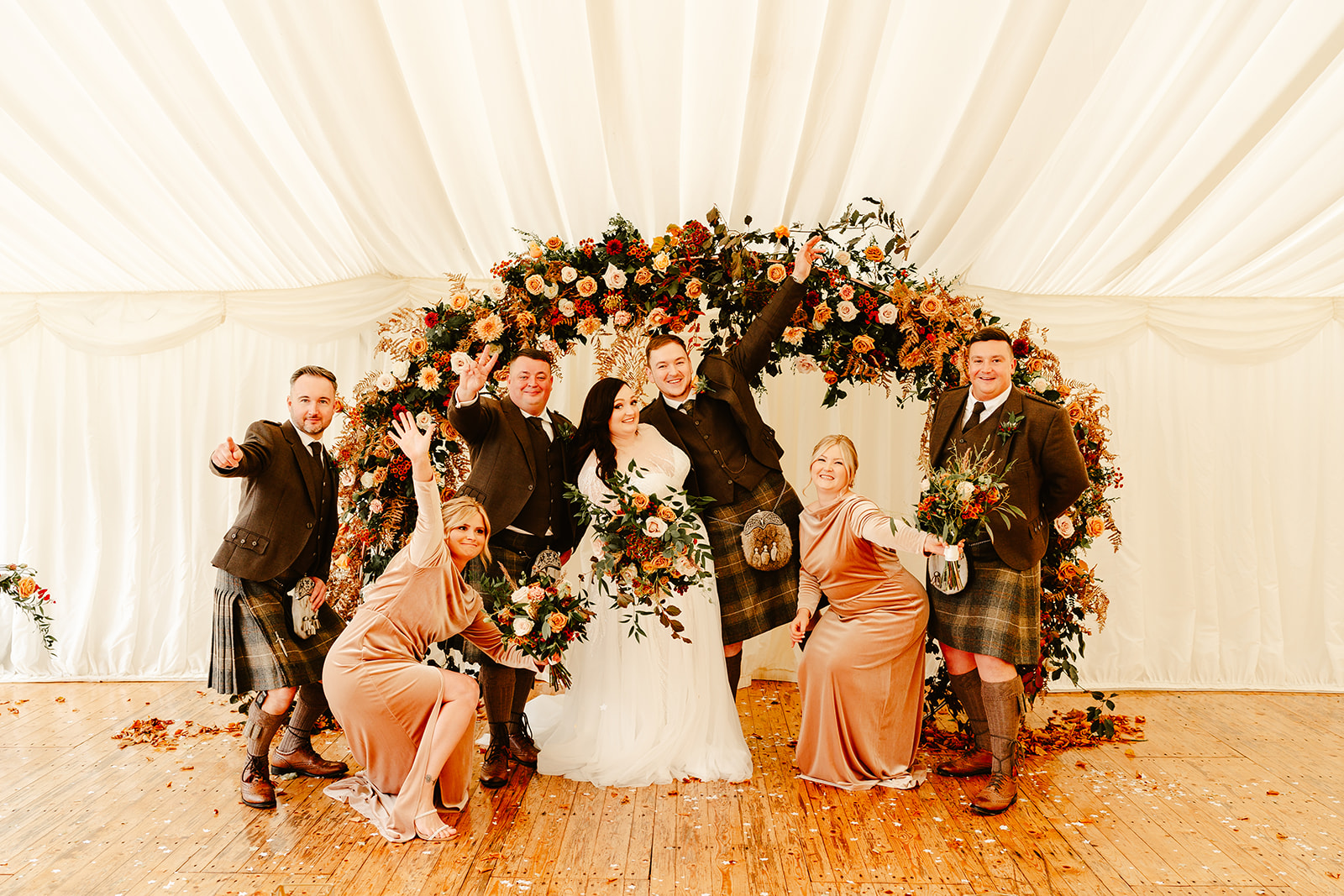 bridal party strike fun poses in front of floral arch inside a marquee at Ballogie House